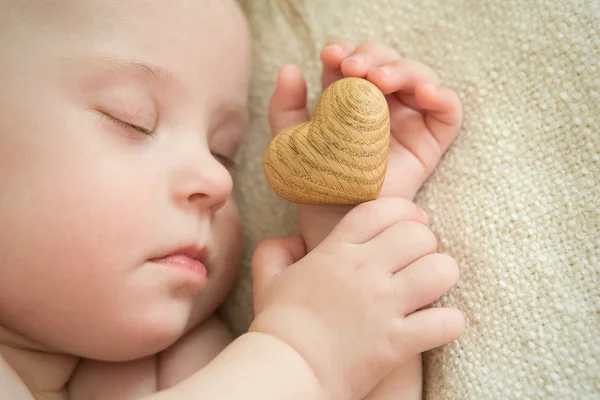 Lilla flicka sover med ett trä hjärta i hand — Stockfoto