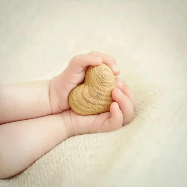 Μικροσκοπικά χέρια μωρού για να κρατήσει την ξύλινη καρδιά — Φωτογραφία Αρχείου