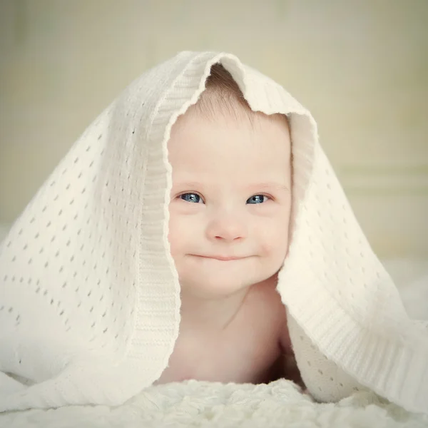 Baby mit Down-Syndrom versteckt sich unter Decke und lächelt verschmitzt — Stockfoto