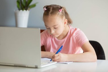 A girl with Down syndrome does her homework at home, prepares her hand for writing, prepares to go back to school. Working out while sitting at a laptop
