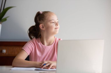 A girl with Down syndrome does her homework at home, prepares her hand for writing, prepares to go back to school. Working out while sitting at a laptop