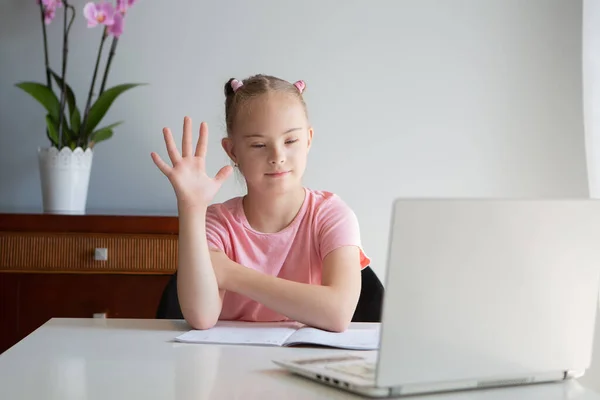 A girl with Down syndrome does her homework at home, prepares her hand for writing, prepares to go back to school. Works out sitting at a laptop. Greets the teacher.