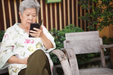 Asyalı, yaşlı, yaşlı, yaşlı, yaşlı bir kadın dışarıda akıllı cep telefonuyla konuşuyor.