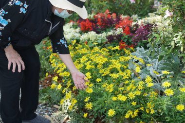 old senior woman wearing facial mask relaxing in flower garden