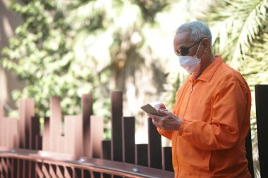 Asya 'lı yaşlı, kıdemli bir adam dışarıda cep telefonu kullanarak maske takıyor. olgun emeklilik yaşam tarzı