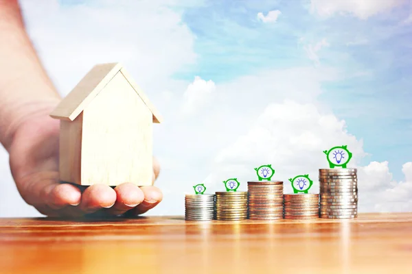 coins stack on wood table with hand holding model wood home with icon piggy bank focus on foreground, idea saving concept focus on fore ground