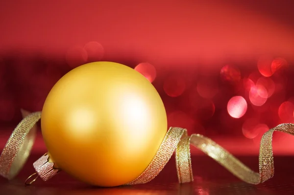 Golden xmas ball and ribbon on the red — Stock Photo, Image