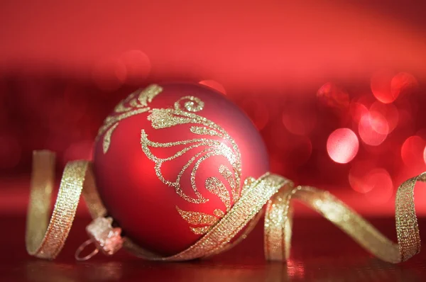 Red xmas ball with golden ribbon on red blurred background — Stock Photo, Image