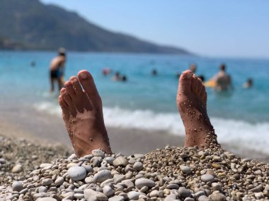 Ayakları deniz taşlarının üzerinde, gökyüzüne karşı. Göğüs uçları olmayan erkek bacakları. Deniz kıyısında ayaklar.