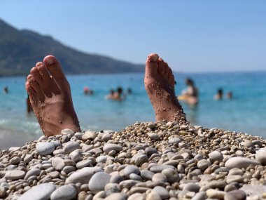 Ayakları deniz taşlarının üzerinde, gökyüzüne karşı. Göğüs uçları olmayan erkek bacakları. Deniz kıyısında ayaklar.