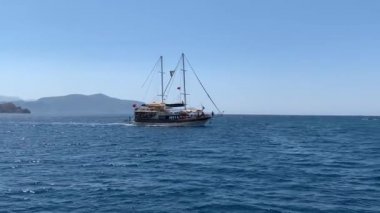 Denizde yelken açan bir gemi var. Gemi tam hızda denizde. Yat adanın yakınından geçiyor. Oludeniz 'den 12 ada turu - Fethiye, Türkiye, 10 Ağustos 2021.
