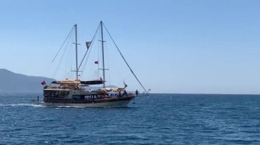 Denizde yelken açan bir gemi var. Gemi tam hızda denizde. Yat adanın yakınından geçiyor. Oludeniz 'den 12 ada turu - Fethiye, Türkiye, 10 Ağustos 2021.