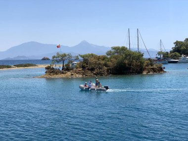İnsanlar denizde bir motorlu tekne ile seyahat ediyorlar. Motorlu bir tekne denizde iz bırakır. Motorlu bir teknenin dümeninde bir adam. Türkiye, Oludeniz - Fethia 12 Adalar Turu, 9 Ağustos 2021