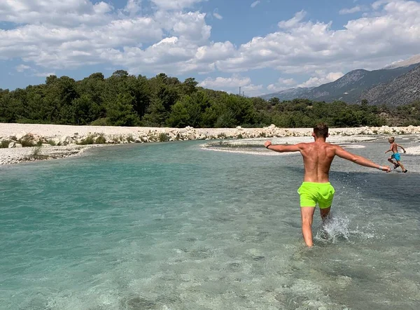 男は川岸を走っている 山の背景に山の川で泳ぐ 子供たちは山の貯水池で泳ぐ トルコ Oludeniz 2021年8月9日 — ストック写真