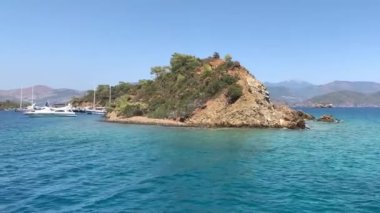 Akdeniz 'de ıssız bir ada. Dağların arka planına ve açık denize karşı kıyıya. Denizle çevrili adalar, yatlar için sakin bir liman. Türkiye, Fethia, 12 ada turu, 9 Ağustos 2021.