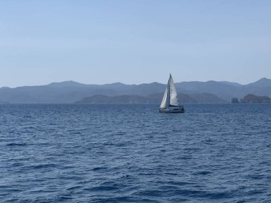 Yacht with a white sail on the high seas. A boat with a sail on the waves of a calm sea. A sailboat floats in the ocean off the coast.