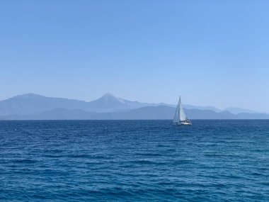 Yacht with a white sail on the high seas. A boat with a sail on the waves of a calm sea. A sailboat floats in the ocean off the coast.
