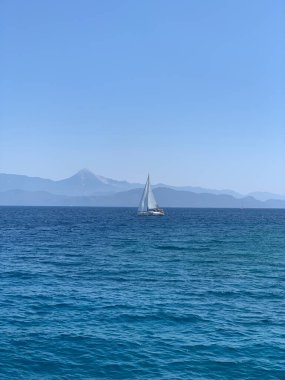 Yacht with a white sail on the high seas. A boat with a sail on the waves of a calm sea. A sailboat floats in the ocean off the coast.