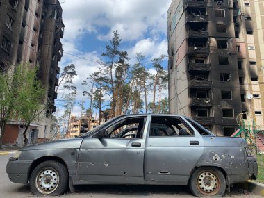 Yıkılan binaların arka planında yanmış ve bomboş bir araba. Evin kalıntıları ve arabanın gövdesinde kurşun izleri var. Rusya ve Ukrayna arasındaki savaş, Irpin-Bucha, 10 Nisan 2022