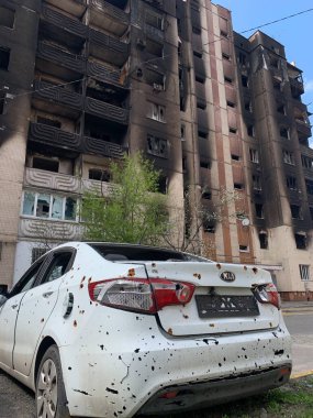 Yıkılan binaların arka planında yanmış ve bomboş bir araba. Evin kalıntıları ve arabanın gövdesinde kurşun izleri var. Rusya ve Ukrayna arasındaki savaş, Irpin-Bucha, 10 Nisan 2022