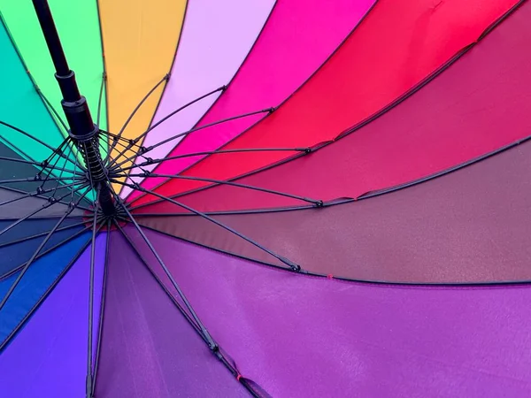 An open umbrella is bright, multi-colored, close-up. Large rain umbrella, all colors of the rainbow. Background texture: umbrella mechanism.