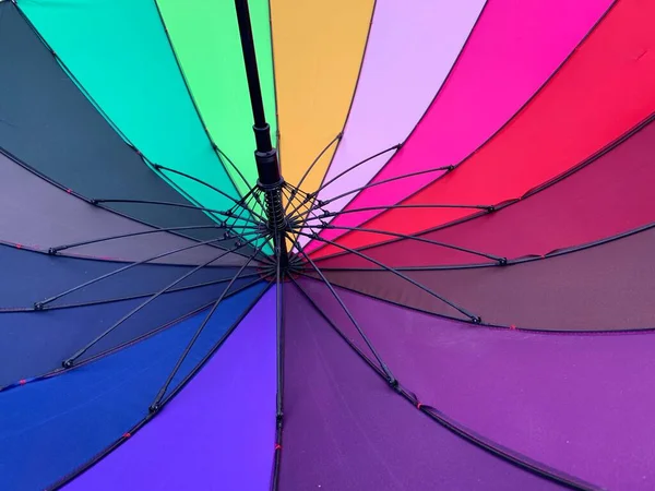 An open umbrella is bright, multi-colored, close-up. Large rain umbrella, all colors of the rainbow. Background texture: umbrella mechanism.