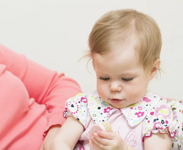 Baby overweegt een haarborstel. — Stockfoto