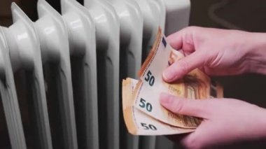 Eller, petrol dolu bir mobil ısıtıcının arka planına karşılık bir tomar para sayıyor. Pahalı elektrik..