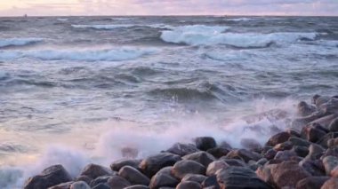 Deniz suyu, güzel gün batımı gökyüzü ve bulutlarıyla bir kaya plajına sıçrar. Deniz dalgası yazın deniz kıyısındaki taşa vurur..