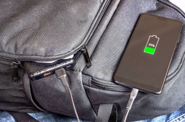 Akıllı telefon, yanında sırt çantasında duran güç bankasından şarj edilir. Modern teknoloji kavramı