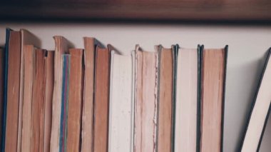 Kütüphane ya da arşivdeki bir rafta düzenlenmiş bir dizi eski kitap. Kamera kitaplık boyunca hareket eder.