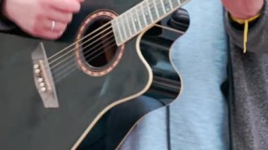 Adam sokakta modern bir gitarda pena çalıyor. Eller yakın çekim..