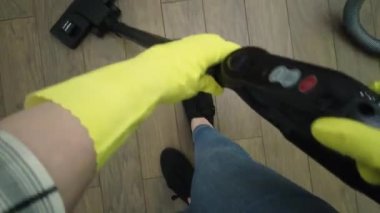 Temizlikçi kadın elektrikli süpürgeyle yerleri süpürüyor, birinci şahıs görüşüyle. Sarı eldivenli eller. POV