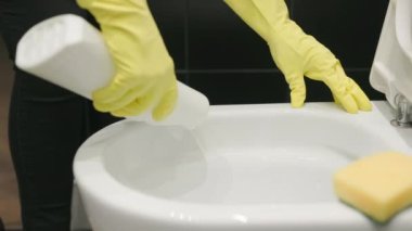 Temizlikçi kadın deterjan ve bez ile tuvaleti temizliyor. Sarı eldivenli eller..