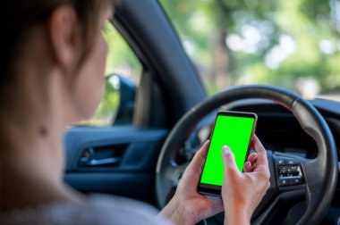 Arabada yeşil ekranlı bir telefon tutan kadın. İş kadını arabada telefonla oturuyor..