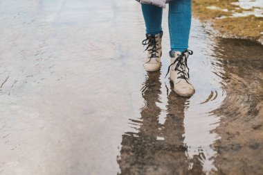 Bir kadın su birikintisine basıyor. Ayaklarının altından su damlaları saçılıyor..