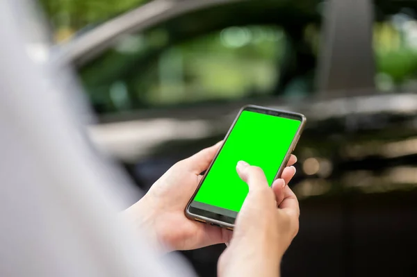 A woman is holding a phone with a green screen on the background of the car. a business woman stands with a phone by the car.