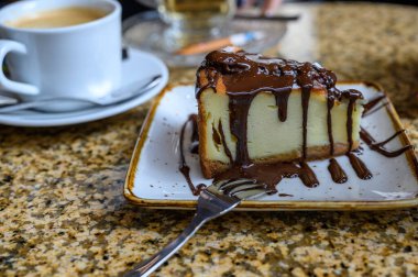 Çikolatayla kaplı cheesecake ve bir kafedeki masada bir fincan kahve..