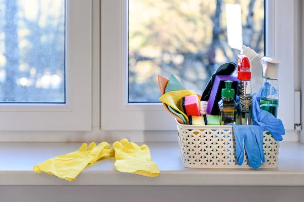 Pencerenin kenarında deterjan, fırça, sünger ve lastik eldivenlerle dolu plastik bir sepet var..