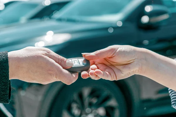 Smart car key on a person\'s hand. Hands of a dealer giving car systems key to a female buyer outdoors.