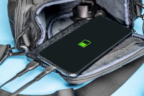 Smartphone charging. The mobile phone is charged from the power bank lying on the backpack.