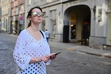 Kız elinde akıllı bir telefon tutarak şehri inceliyor. Bayan bir cep telefonu kullanıyor..