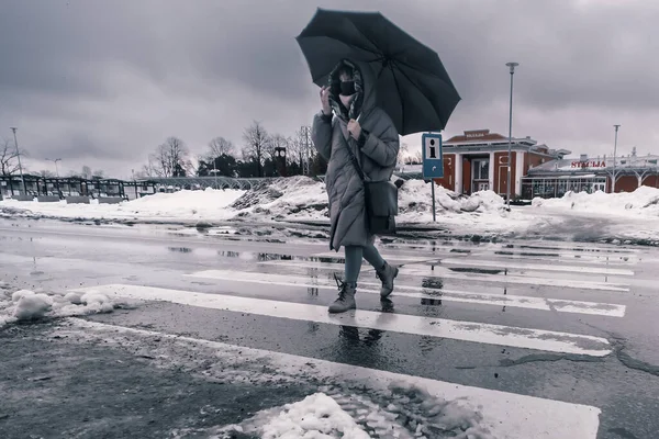 A woman crosses the road in rainy weather with her black umbrella. Bad weather.