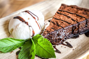 Tahta bir masanın üzerinde nane yapraklarıyla süslenmiş bir parça çikolatalı pasta.