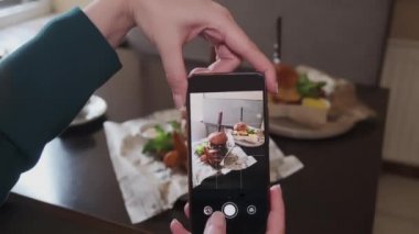 Bir kadın akıllı telefonuyla, sosyal ağlar için bir kafede lezzetli bir hamburgerin fotoğrafını çekiyor..