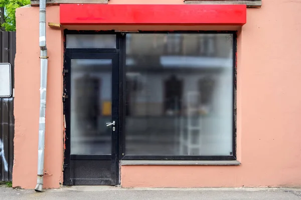 Facade of a small boutique with a large window and a place for a name. Empty showcase.