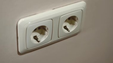 Bir el beyaz bir elektrik prizine şarj aleti yerleştirir..