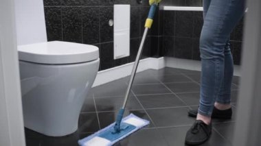 A cleaning lady in yellow gloves washes the floor in the toilet. House cleaning.