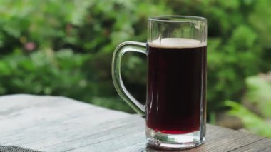 A glass of cold frothy dark beer on the table against the backdrop of nature.