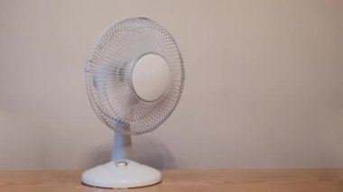 Ev veya ofis için beyaz plastik bir vantilatör bir duvarın arka planında dönüyor.